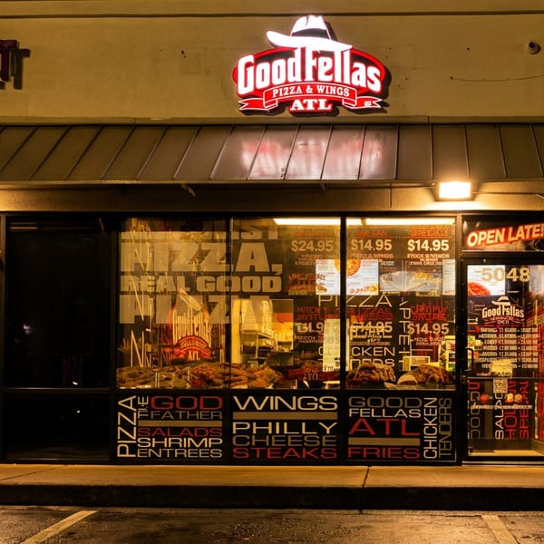 Goodfellas Pizza & Wings ATL storefront at night, with a bright neon sign and menu visible.