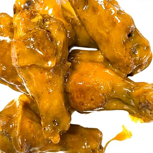 Close-up of several golden-brown chicken wings coated in a thick, glossy sauce on a white background.