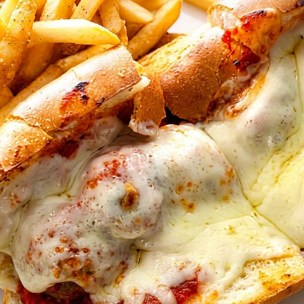 A meatball sub sandwich with melted cheese and marinara sauce, served with a side of french fries.