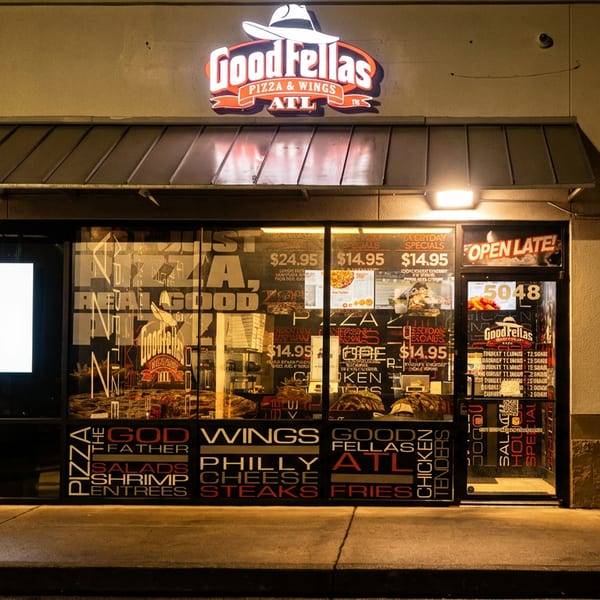 GoodFellas Pizza & Wings ATL storefront at night, with a glowing sign and window advertisements.