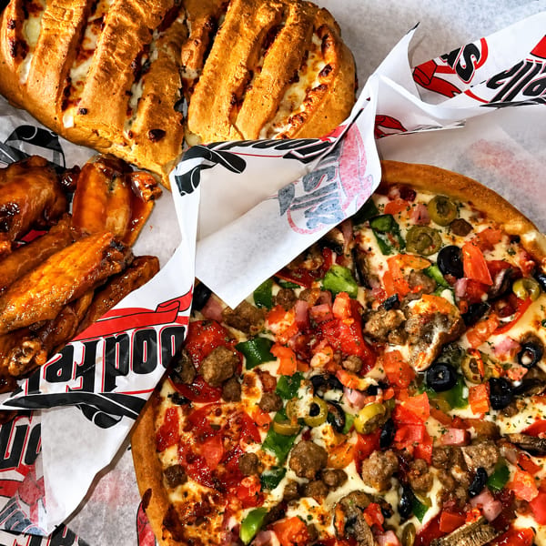 Loaded pizza, cheesy breadsticks, and saucy chicken wings arranged on branded restaurant paper.
